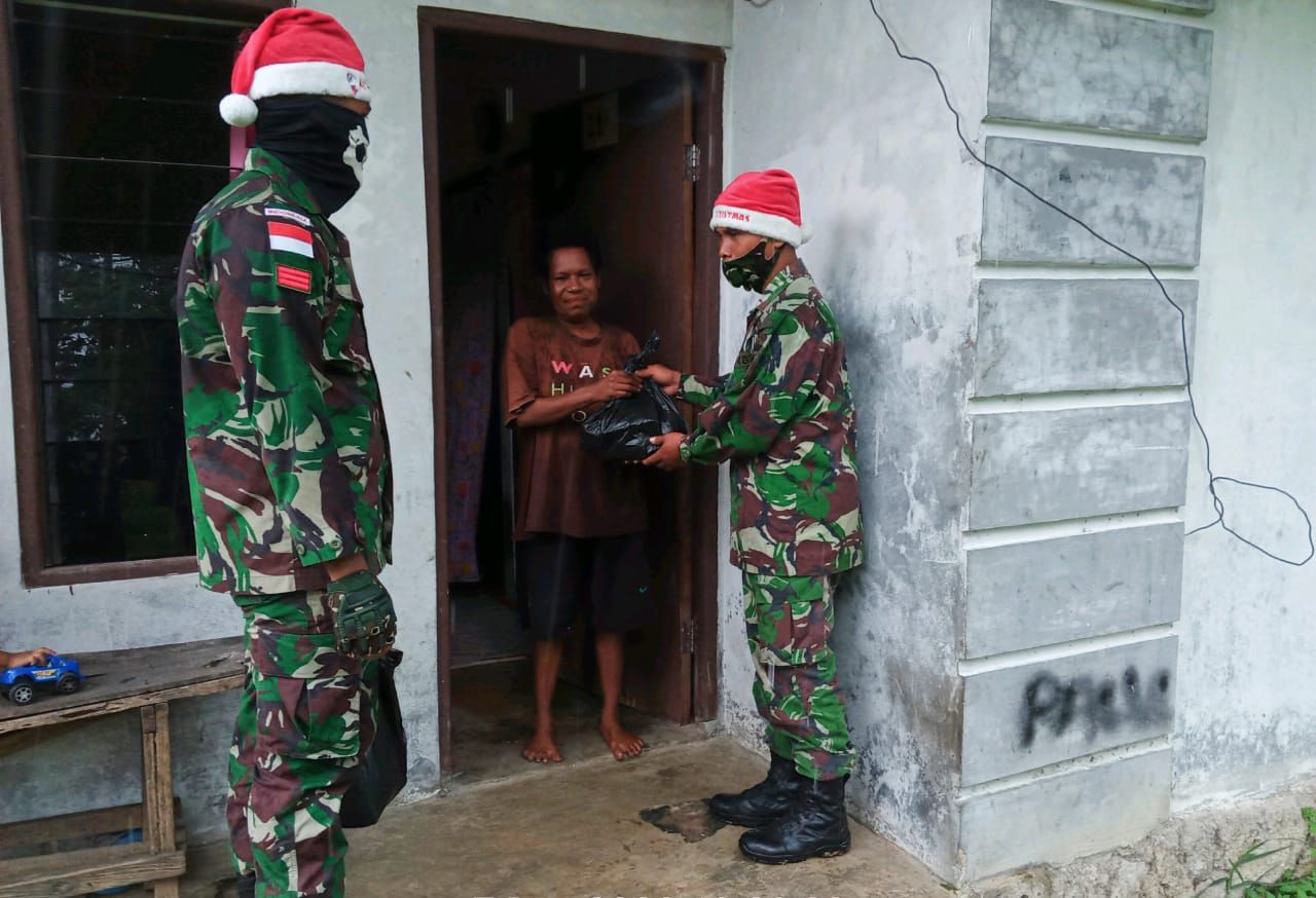 Gunakan Topi Santa Claus, Satgas Yonif Raider 100/PS Pos Workwana Bagikan Sembako Kepada Masyarakat